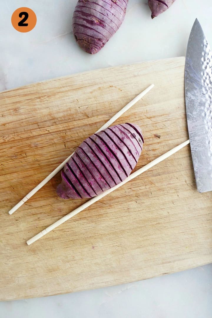 hasselback purple sweet potato in between two chopsticks on a cutting board