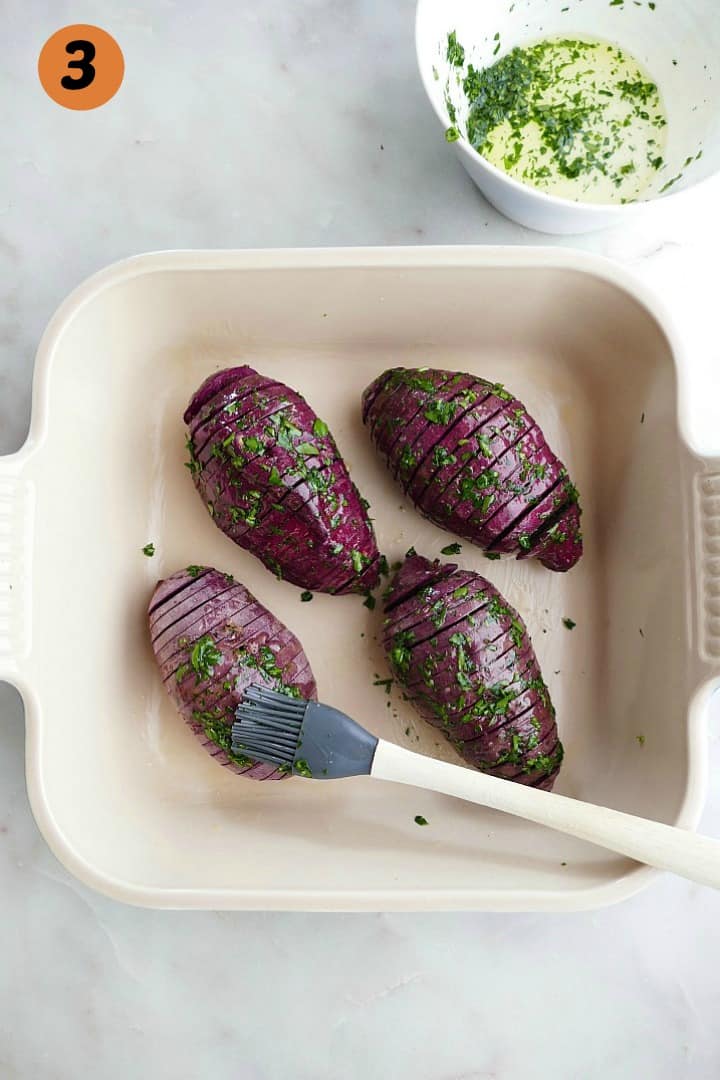 4 hasselback purple sweet potatoes in a square baking dish brushed with seasonings