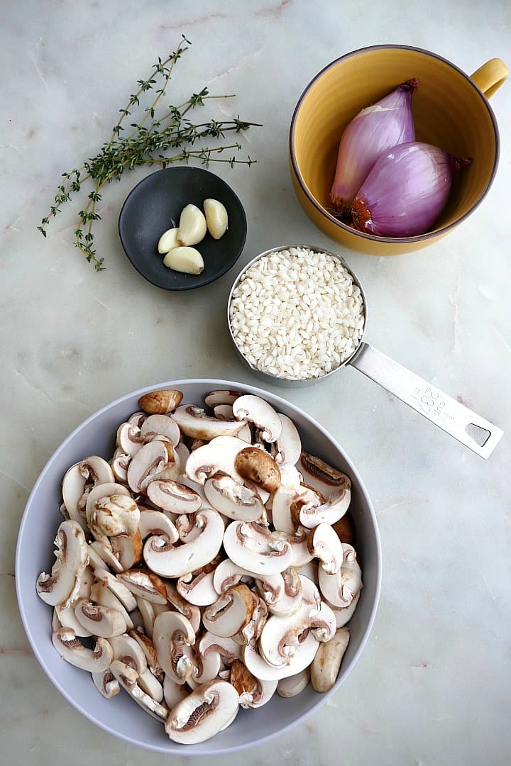 sliced mushrooms, arborio rice, shallots, garlic, and thyme on a white counter