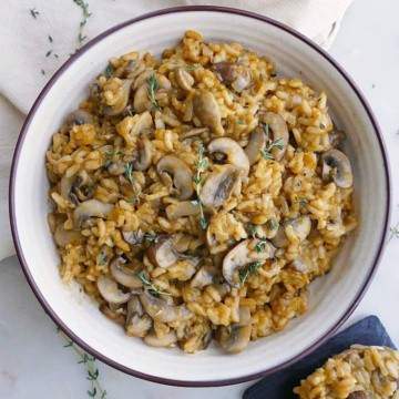 vegan mushroom risotto in a white bowl with thyme on a napkin