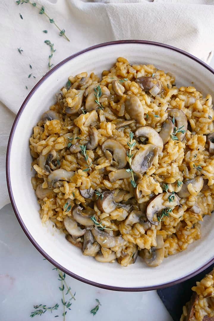 vegan mushroom risotto in a white bowl with thyme on a napkin