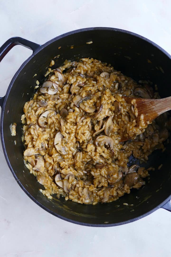 creamy vegan mushroom risotto in a black dutch oven with a wooden spoon