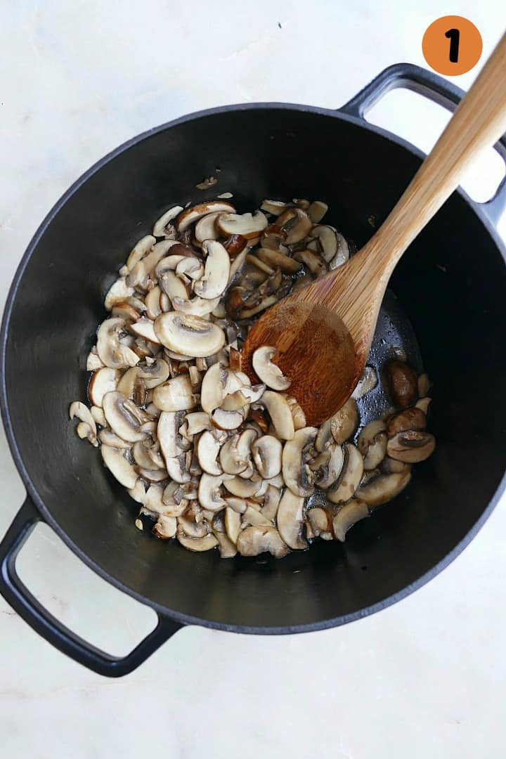 sauteed sliced mushrooms in a black dutch oven with a wooden spoon on a counter