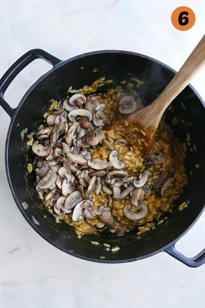 creamy vegan risotto with cooked mushrooms on top in a black dutch oven with a spoon