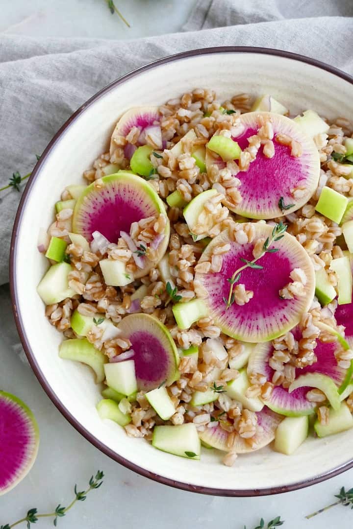 close up of watermelon radish salad topped with thyme in a white bowl