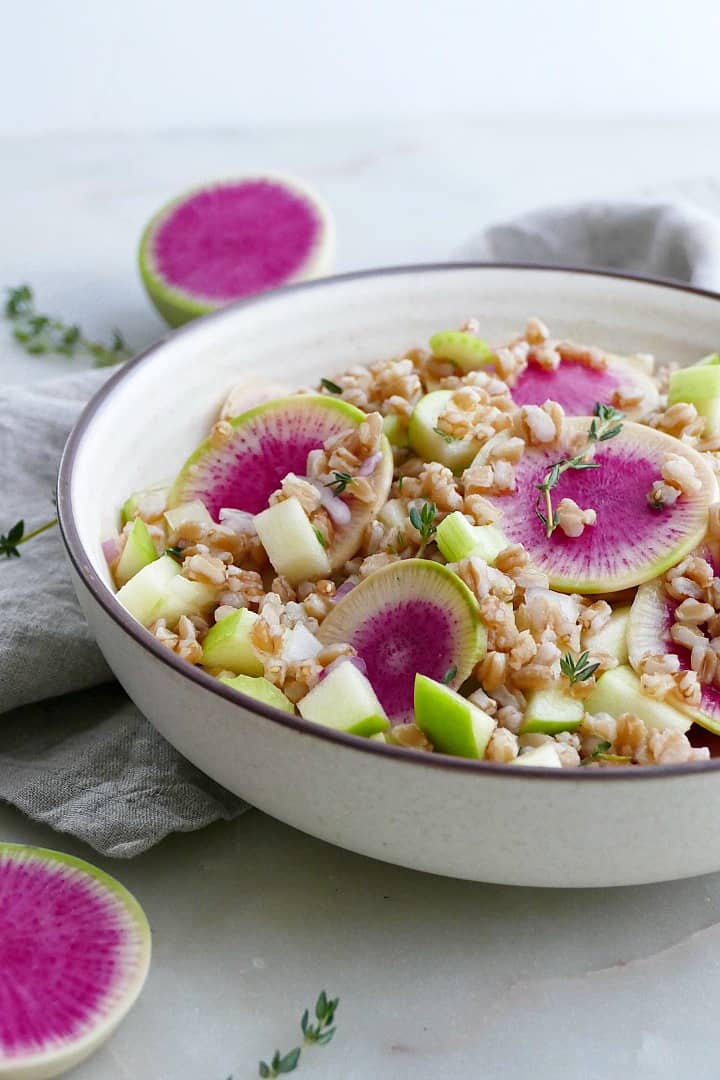 side view of watermelon radish salad with citrus thyme dressing in a white bowl