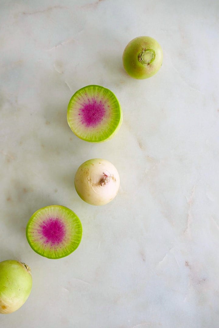 5 watermelon radishes in a slanted line on a white counter top