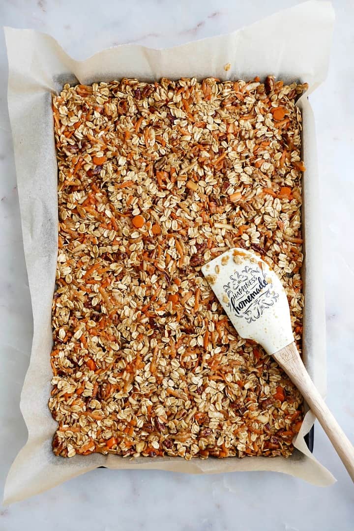 baking sheet with parchment paper and granola spread on top with a white spatula