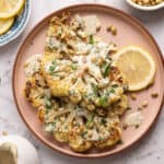 Cauliflower steaks with tahini sauce, pumpkin seeds, and parsley on a serving plate.