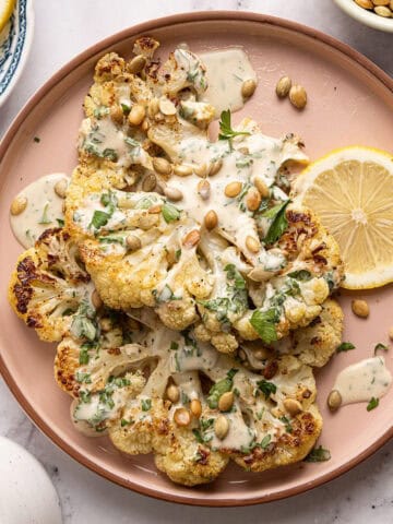Cauliflower steaks with tahini sauce, pumpkin seeds, and parsley on a serving plate.