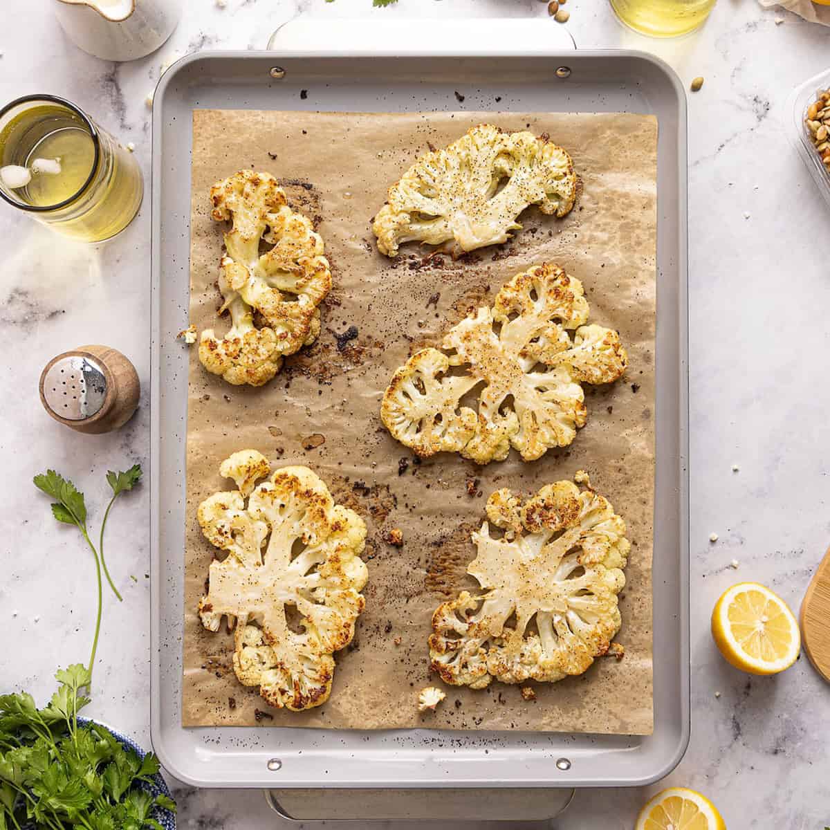 Roasted cauliflower steaks on a baking sheet lined with parchment after coming out of the oven.