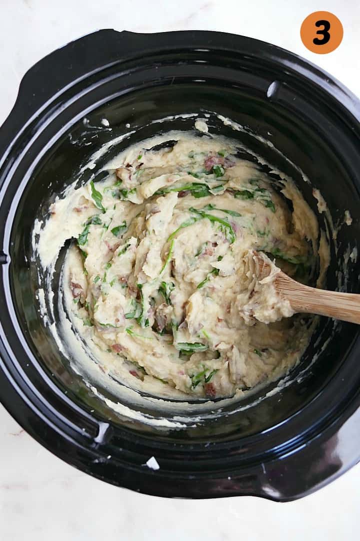 arugula mixed into potatoes prepared in a crockpot with a wooden spoon
