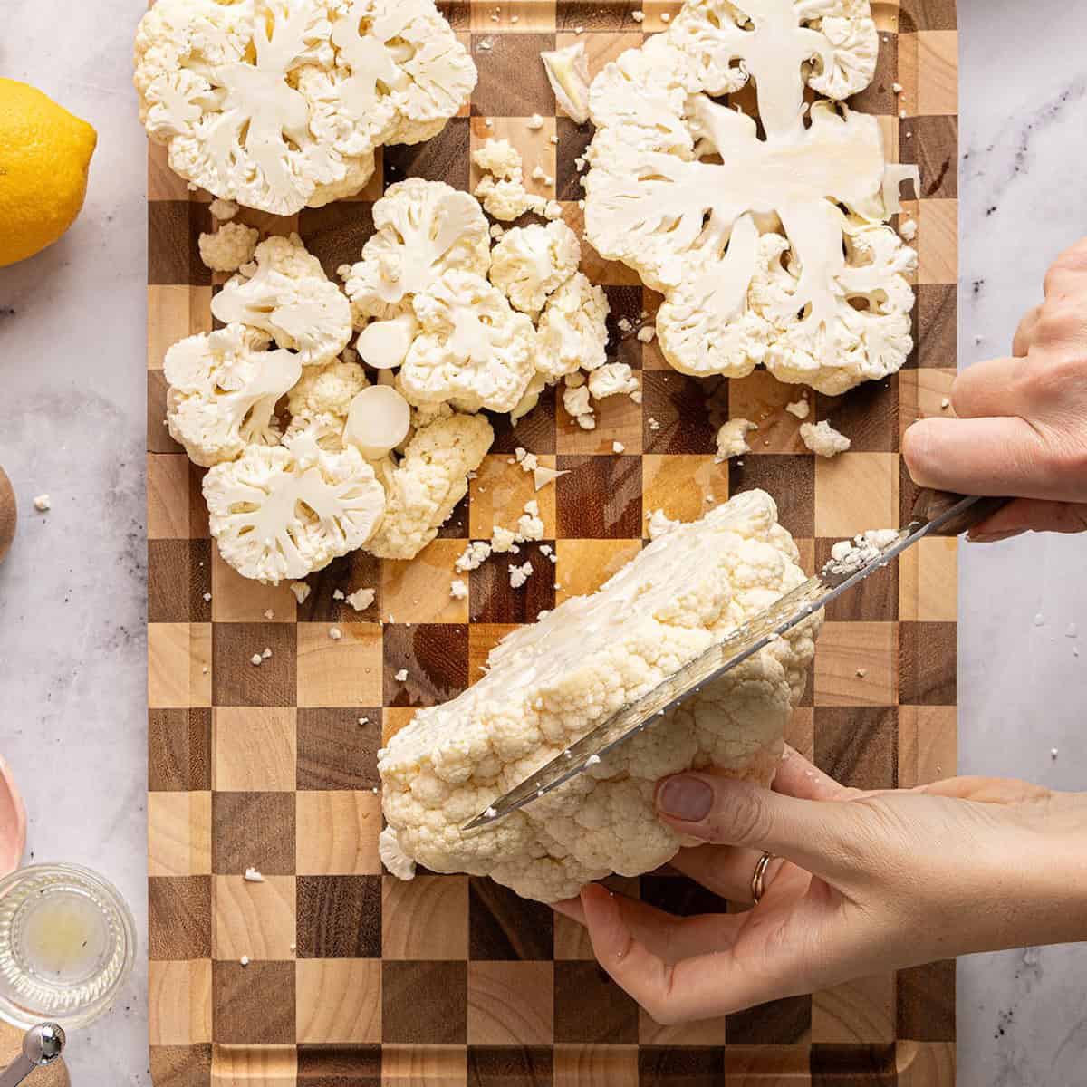 Woman slicing a head of cauliflower into steak pieces on a cutting board.