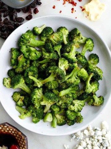 square image of roasted frozen broccoli on a white plate in the middle of five seasonings