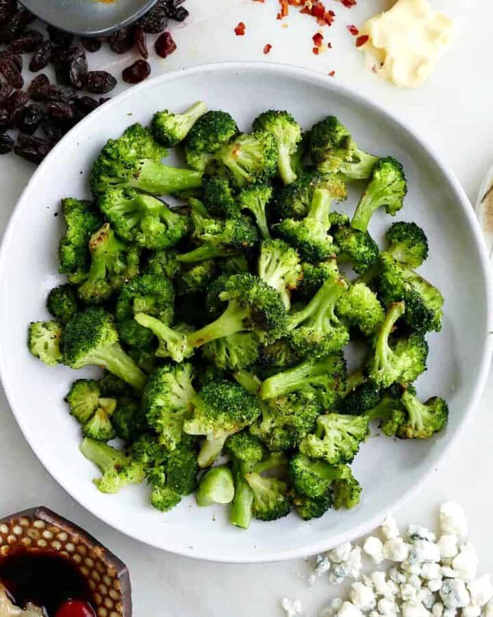 square image of roasted frozen broccoli on a white plate in the middle of five seasonings