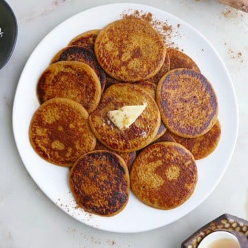 close up of a white plate with several sweet potato pancakes with a slab of butter