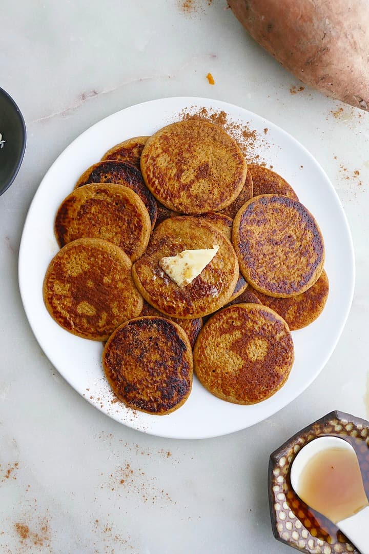 close up of a white plate with several sweet potato pancakes with a slab of butter