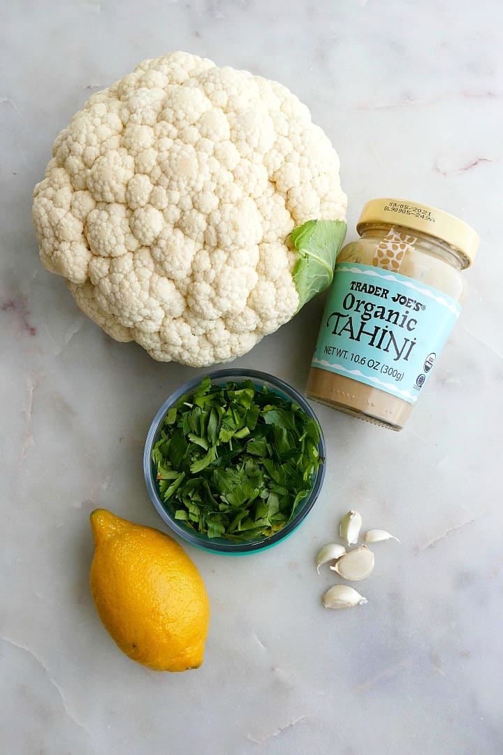 a head of cauliflower, jar of tahini, chopped parsley, a lemon, and garlic cloves