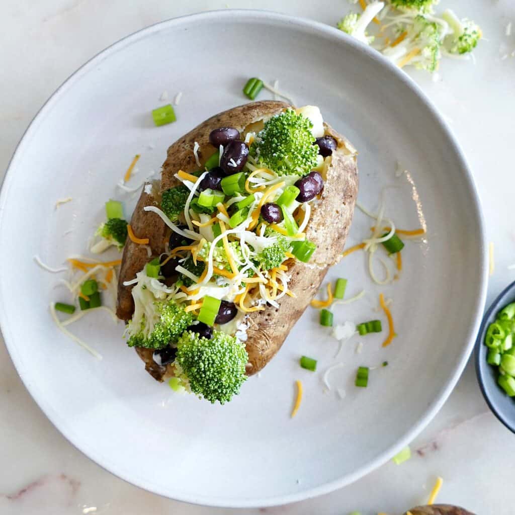 square image of a baked potato with toppings on a white plate