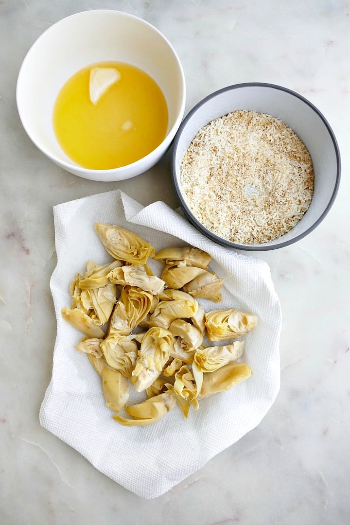 melted butter, breadcrumbs, and artichoke hearts next to each other on a counter