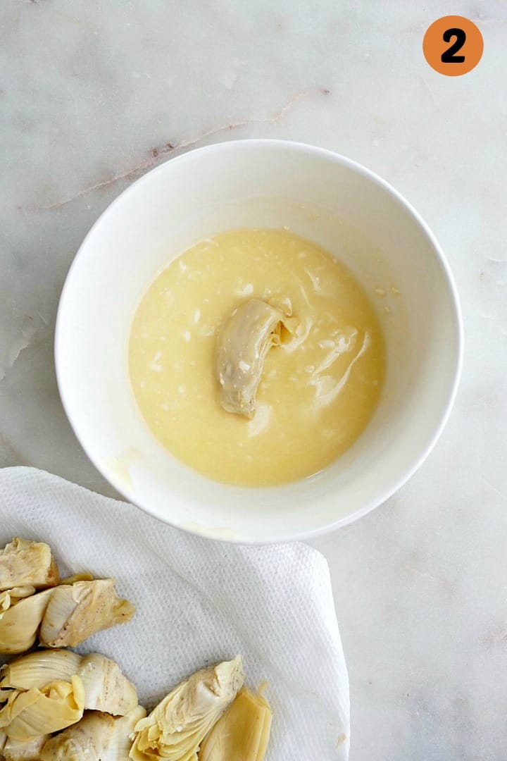 an artichoke heart in a bowl with melted butter on a counter