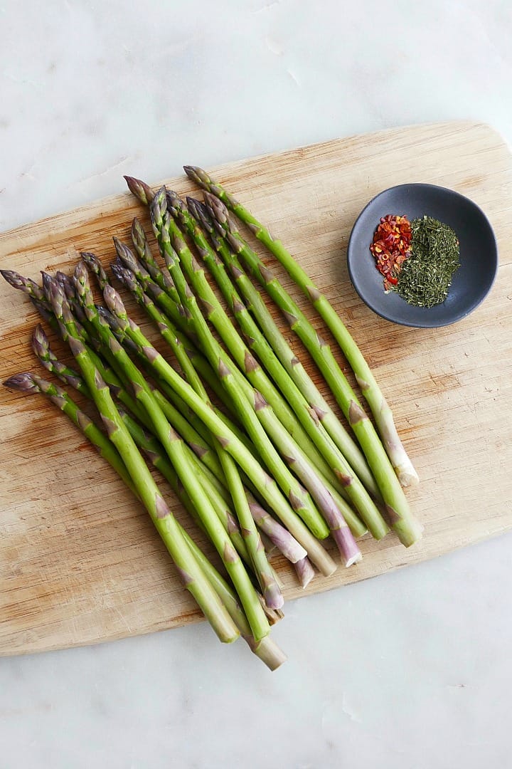 a bunch of asparagus spears spread on a bamboo cutting board next to spices