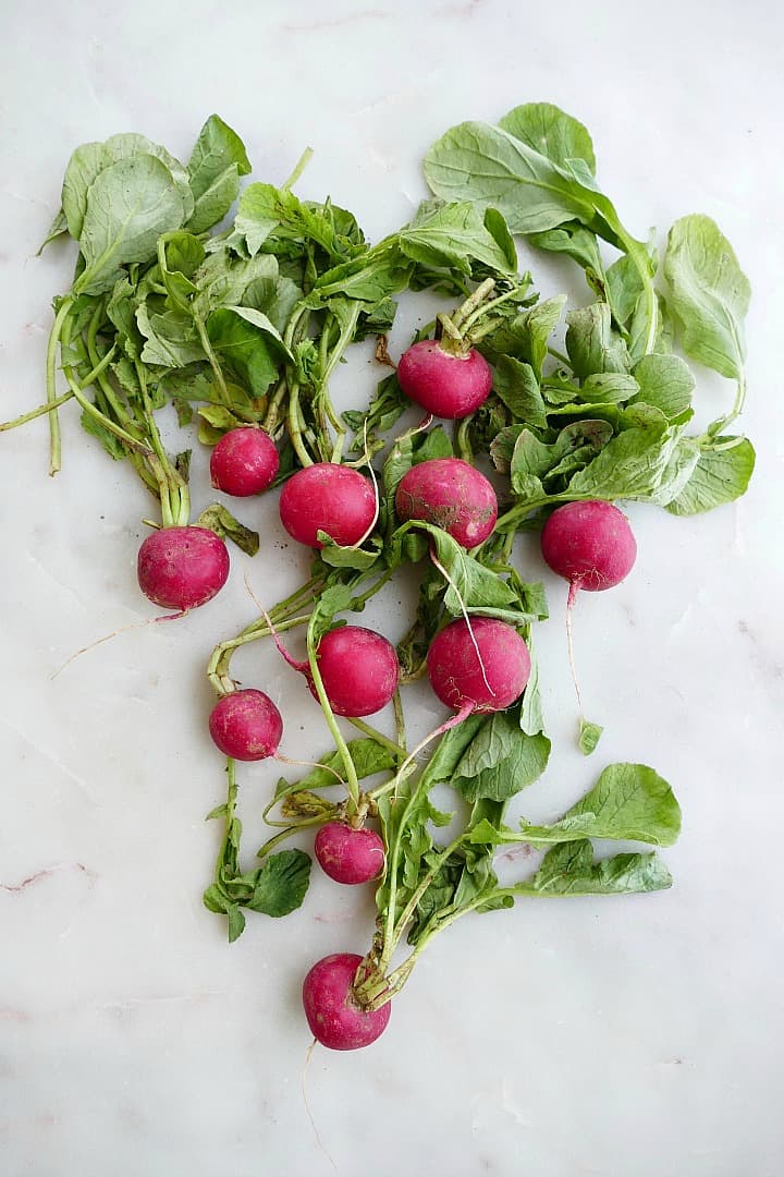 red radishes with their greens spread out on a white counter