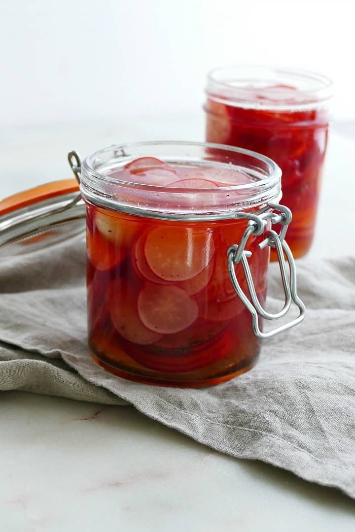 side view of pickled radishes in a glass jar on a gray napkin