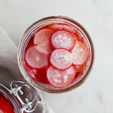 overhead of a glass jar of pickled radishes on a white counter