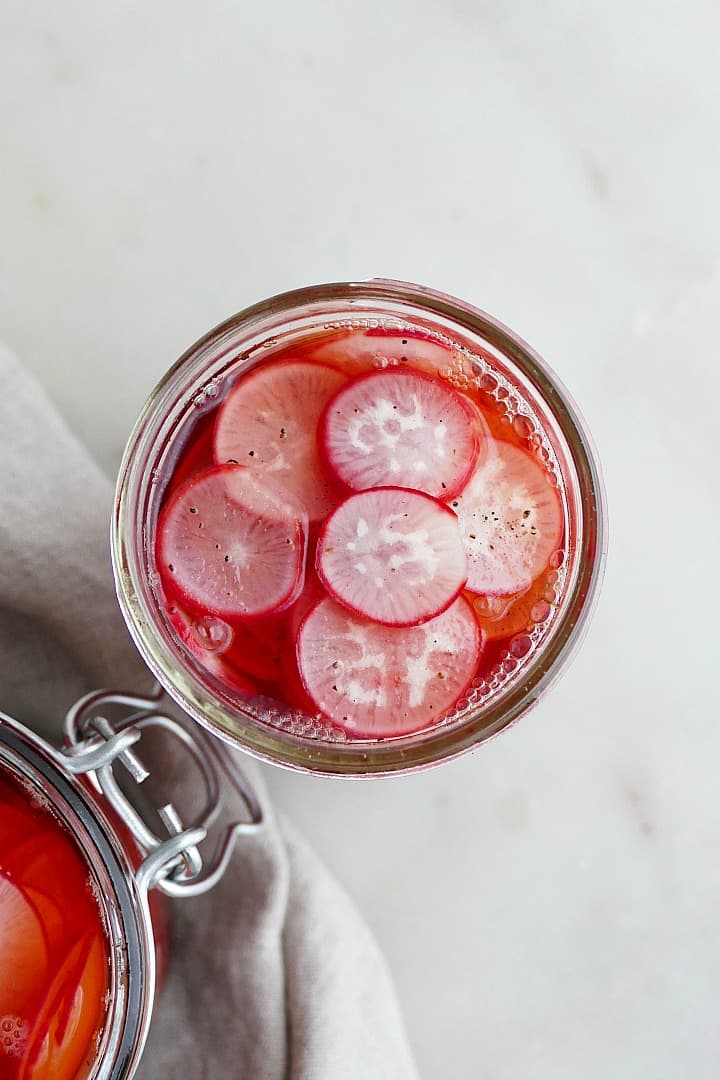 overhead of a glass jar of pickled radishes on a white counter