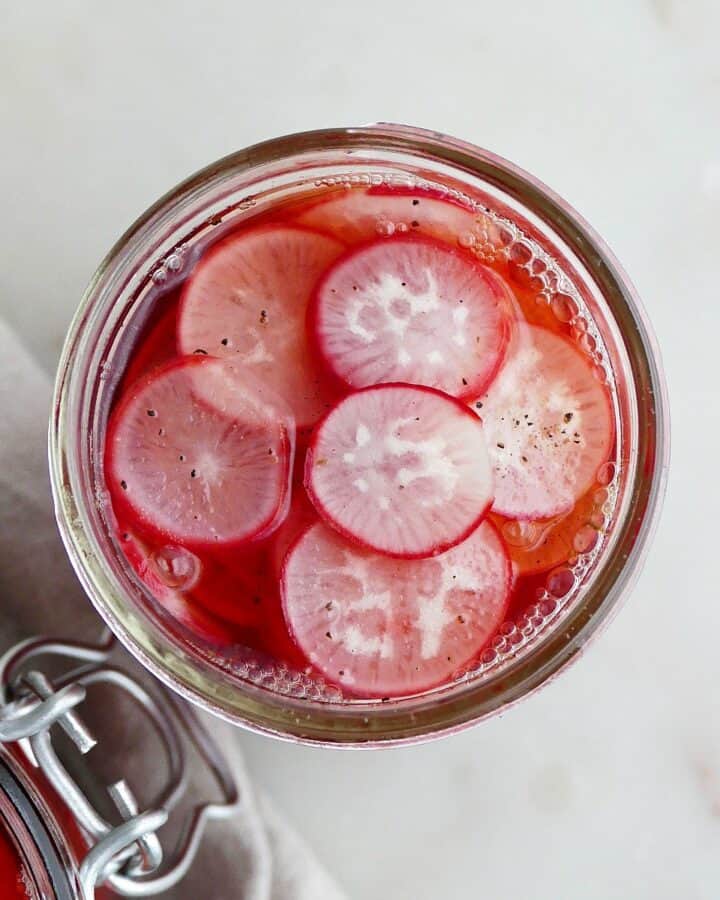 overhead shot of one jar with pickled radishes on a white counter