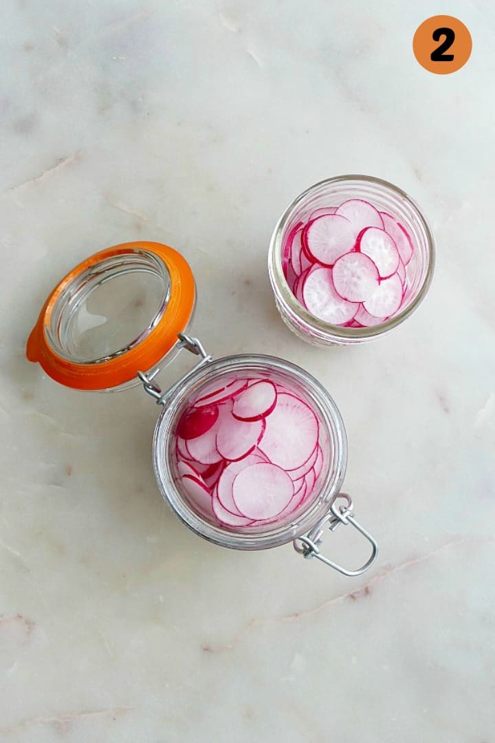 two glass jars full of radishes on a white counter