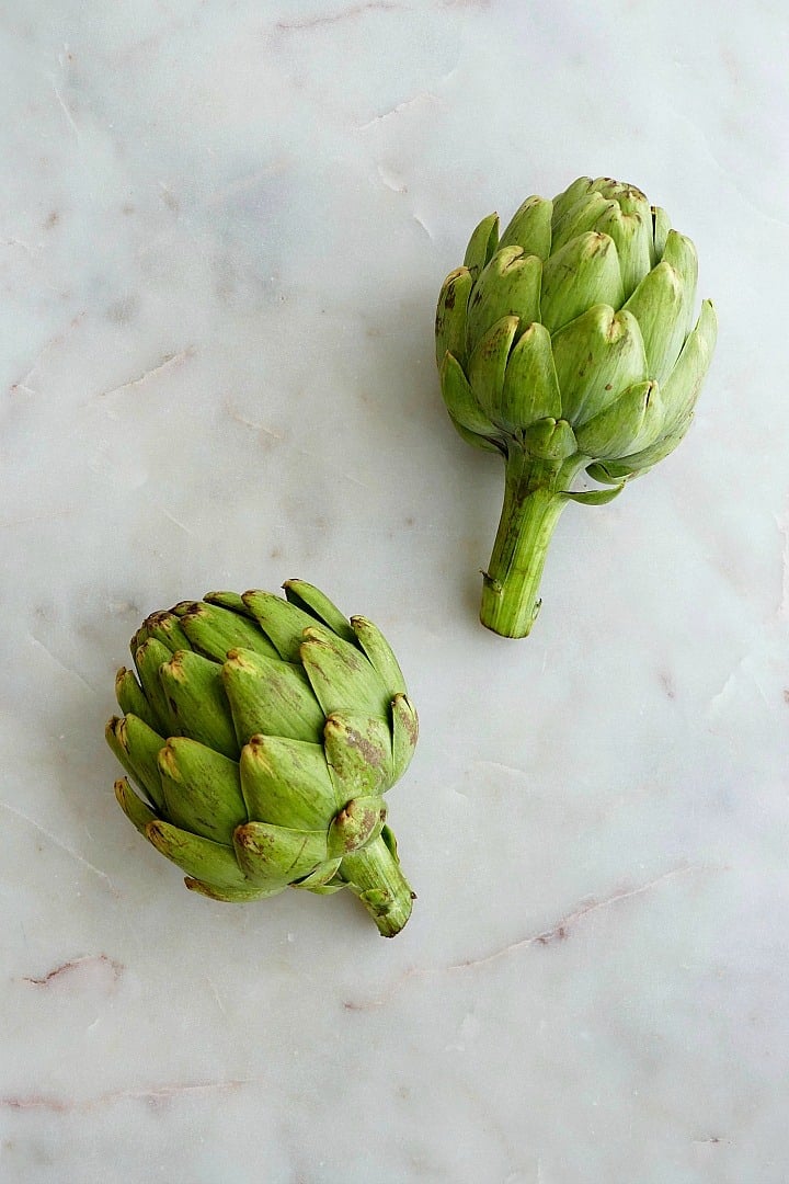 two heirloom artichokes next to each other on a white counter