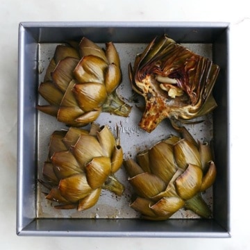 4 artichokes in a square baking dish on a white counter