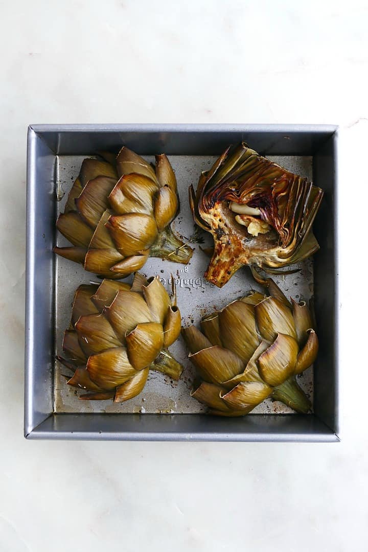 4 artichokes in a square baking dish on a white counter