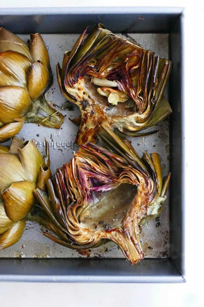 close up of two roasted artichoke halves in a silver baking dish