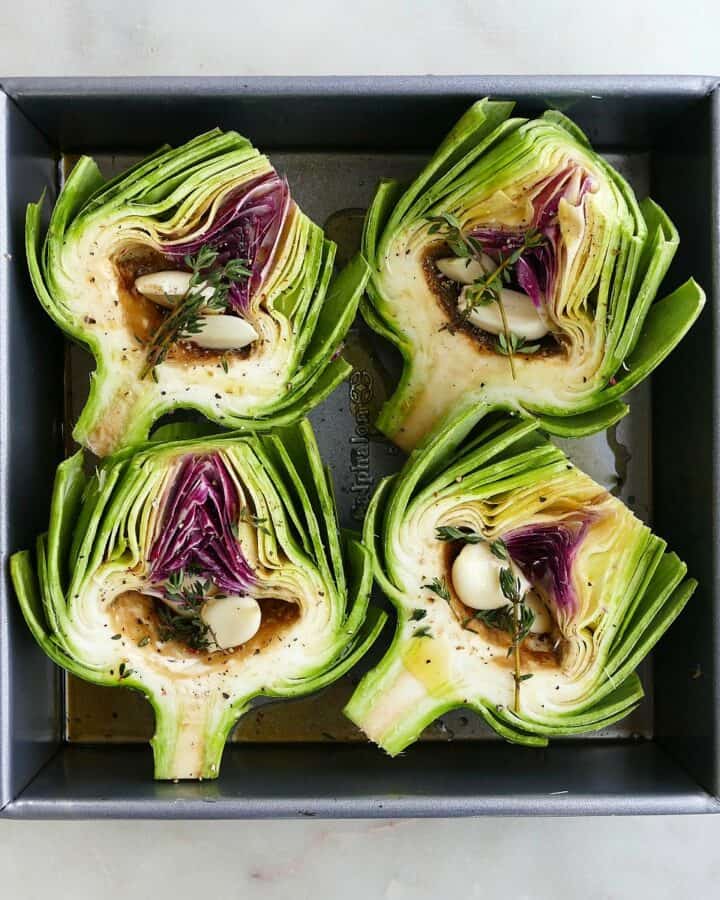 square image of 4 artichoke halves stuffed with garlic in a baking dish