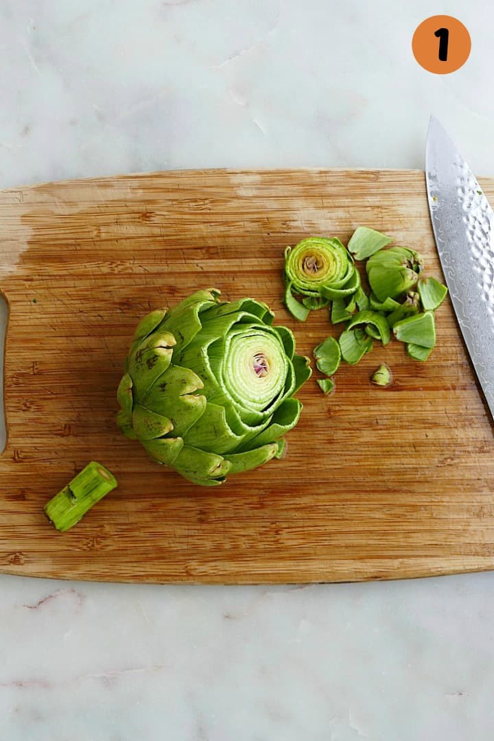 an artichoke with the tip sliced off on a cutting board