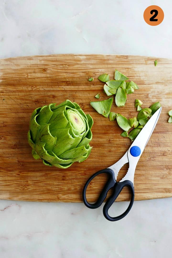 an artichoke next to kitchen scissors on a cutting board