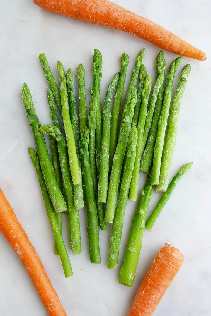 one bunch of asparagus and three carrots spread out on a white counter