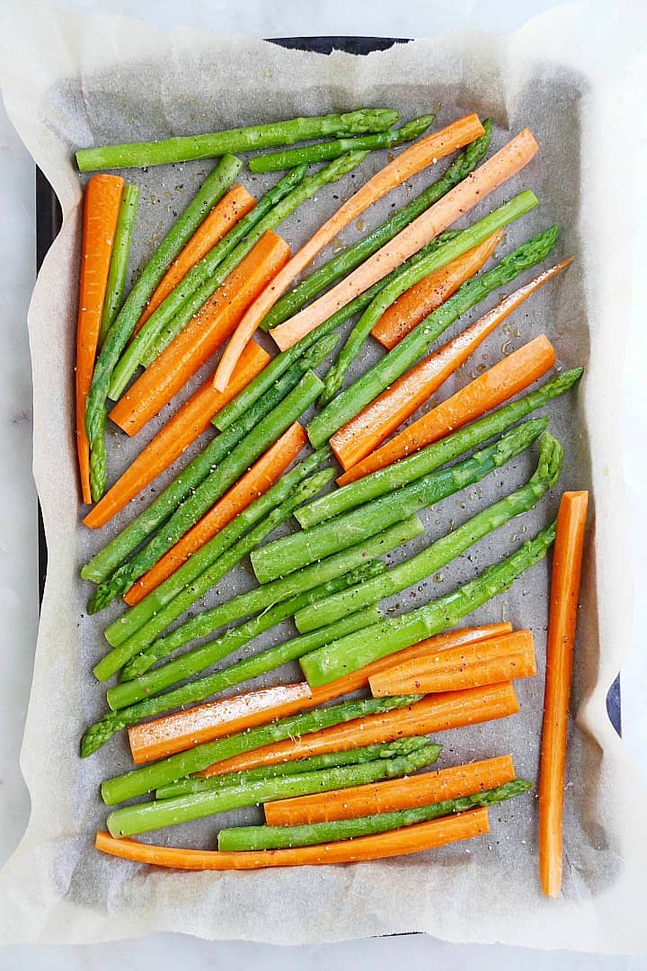 asparagus spears and carrot slices on a baking sheet lined with parchment paper