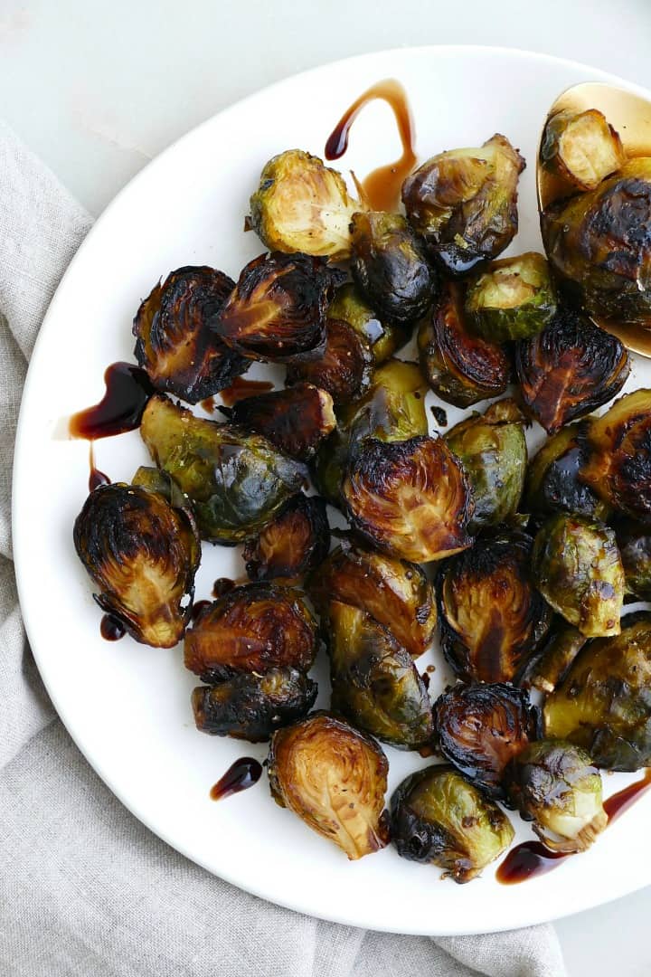 crispy brussel sprouts tossed in balsamic reduction on a white plate