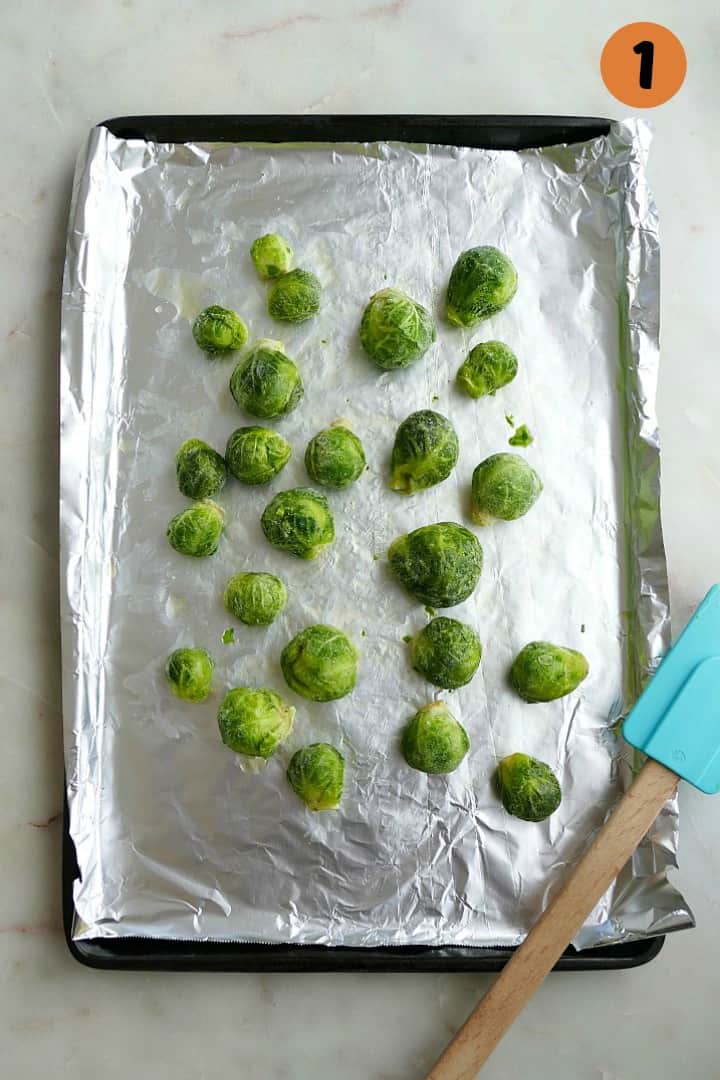 frozen brussels sprouts on a baking sheet lined with aluminum foil and a blue spatula