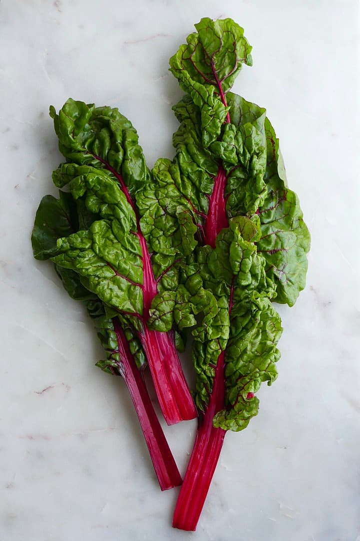 three large pieces of swiss chard with red stems on a white counter