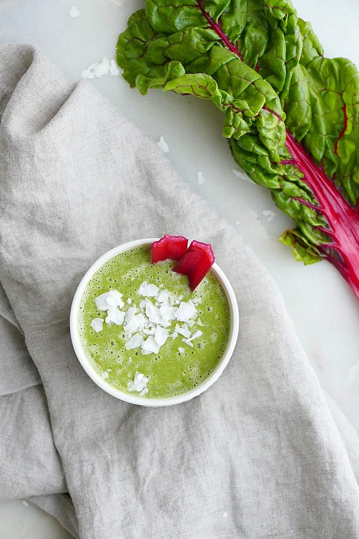 swiss chard smoothie topped with coconut on a gray napkin next to chard leaves