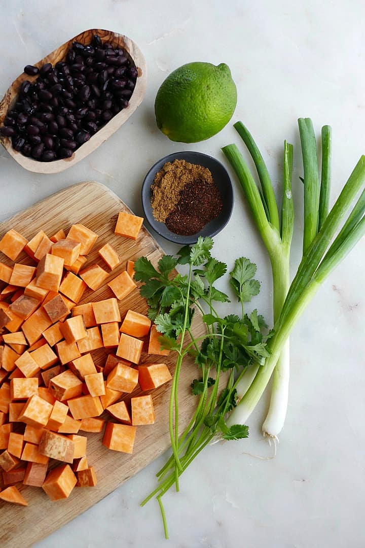 black beans, diced sweet potato, cilantro, scallions, spices, and lime on a counter