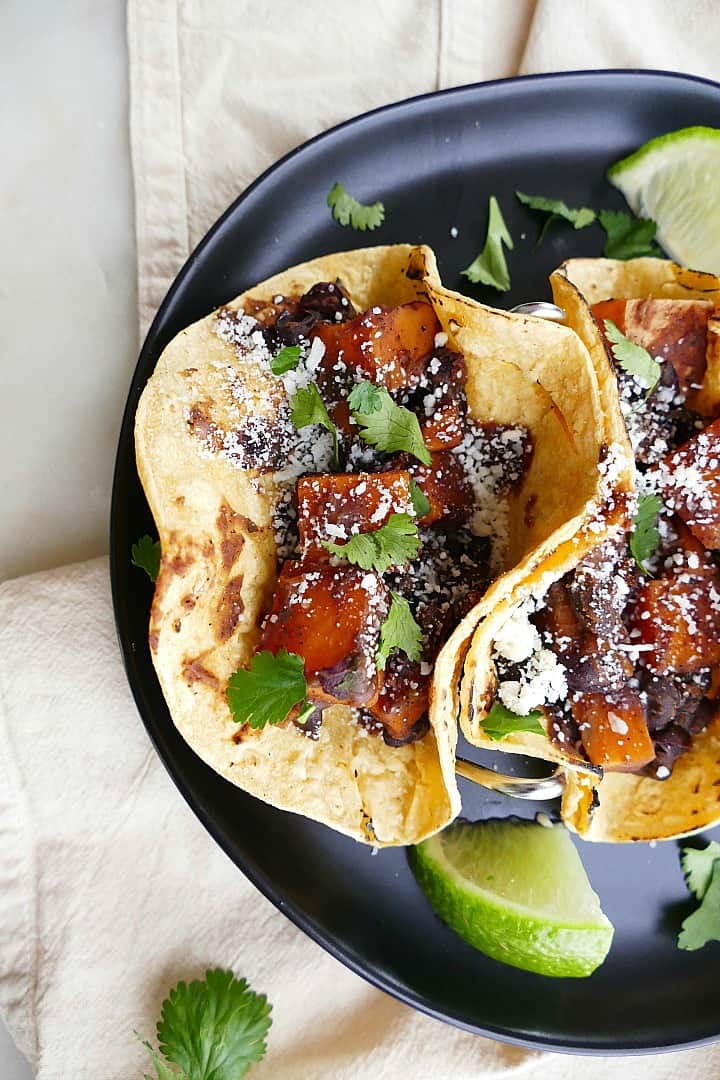 close up of black bean sweet potato tacos on a black plate on a yellow napkin