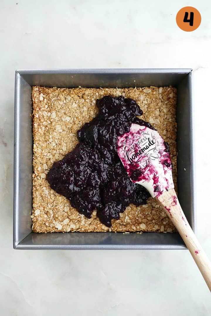 oat base with blueberry rhubarb jam on top and a white spatula in a baking dish
