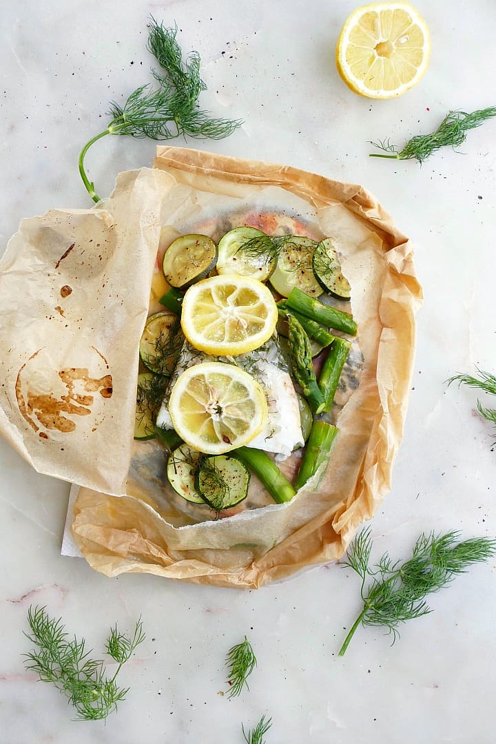 cod en papillote with lemon slices and green vegetables on a white counter