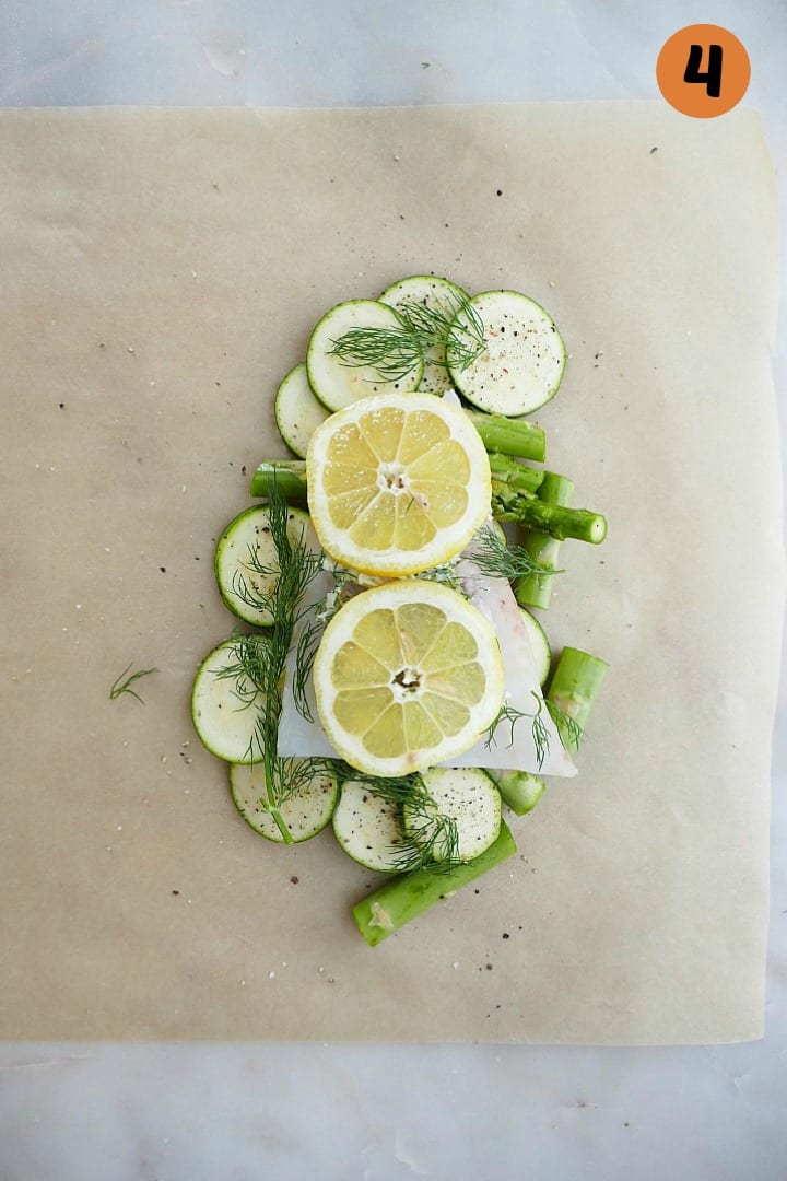 sliced veggies, cod, and lemon slices on a piece of parchment paper on a counter